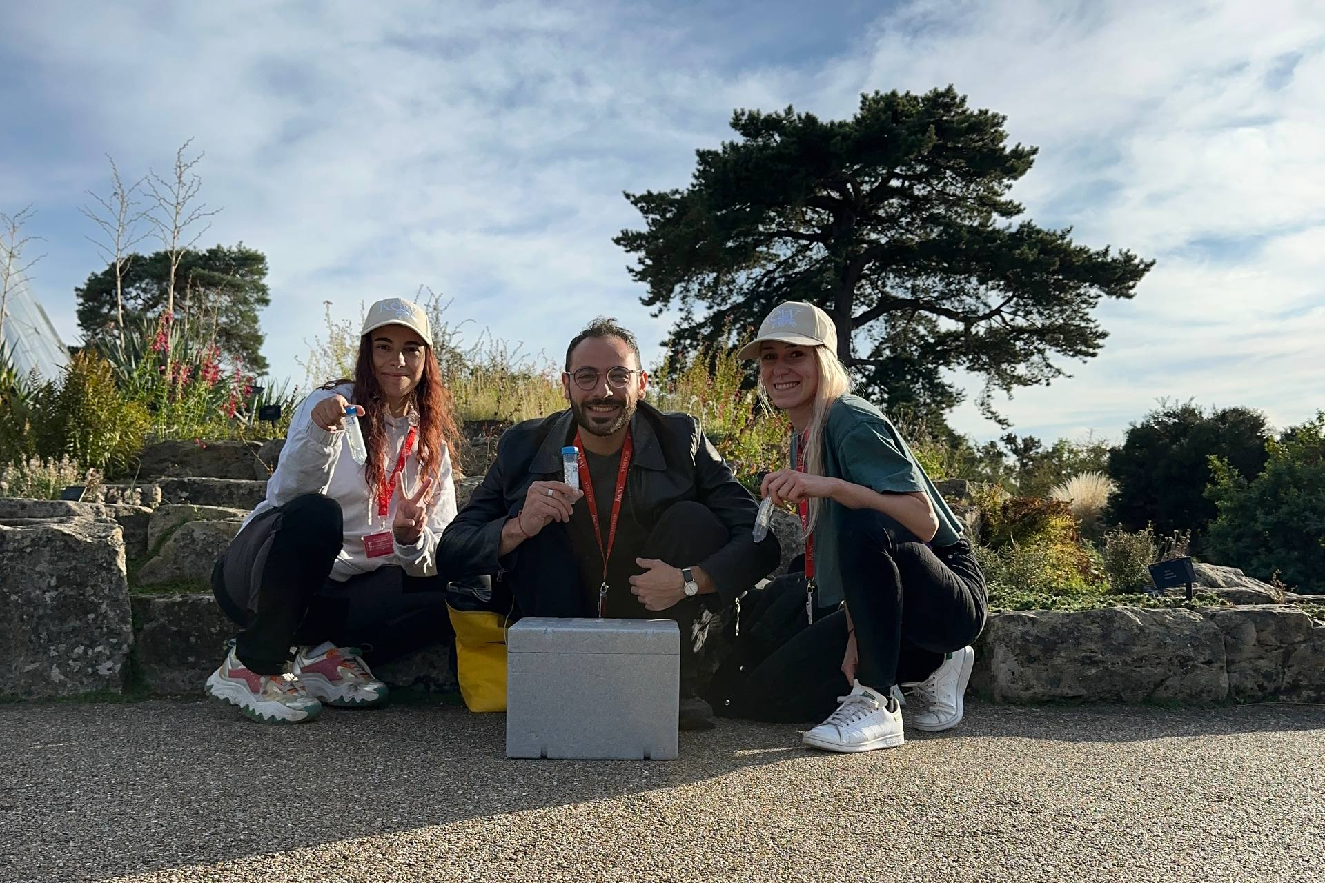 Three researchers crouching on a path at Royal Botanic Gardens, Kew, holding sample vials beside a collection cool-box.