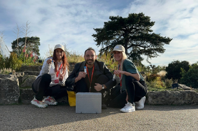 Three researchers crouching on a path at Royal Botanic Gardens, Kew, holding sample vials beside a collection cool-box.